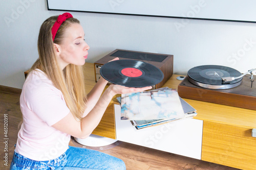 Young woman blowing dust off vinyl record and listening to music on turntable at home