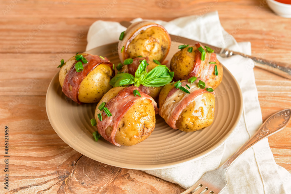 Plate of tasty baked potatoes with bacon on wooden background