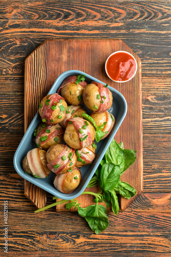Baking dish of tasty baked potatoes with bacon on wooden background