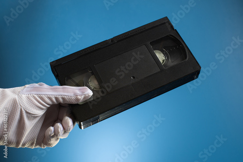 Hand holds retro HVS video cassette on a blue background. Retro wave. 80s 90s