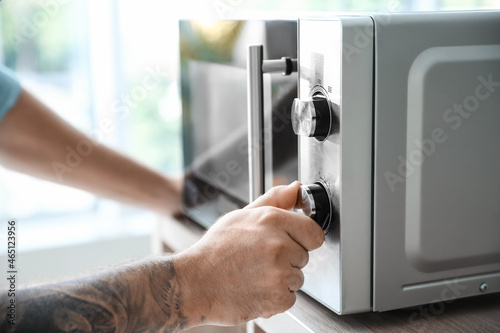 Young man adjusting microwave oven in kitchen, closeup