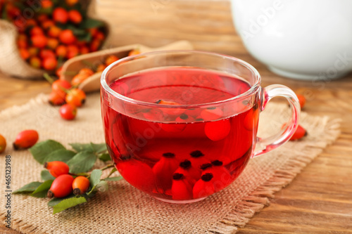 Glass cup of rose hip tea and berries on wooden background