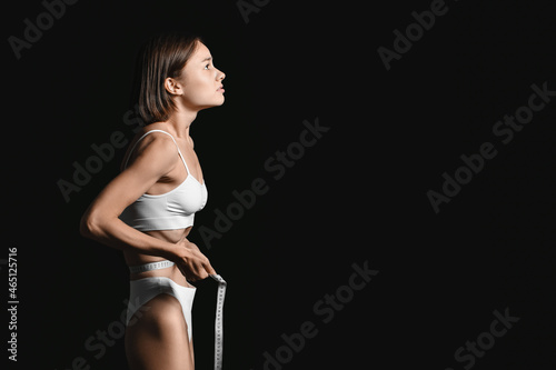 Canvas Print Young woman with measuring tape on dark background