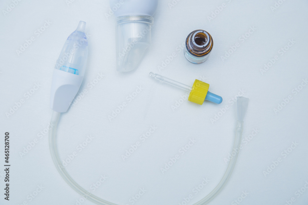 The children's aspirator lies in a semicircle on a white background, to the side of it are drops from a runny nose with a pipette and water for washing. High quality photo