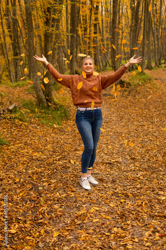 a young blonde girl in a brown knitted sweater in jeans catches falling leaves in the autumn forest