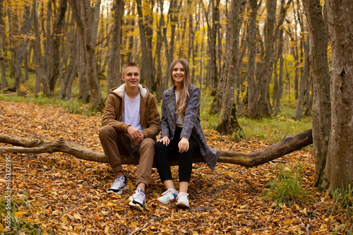 a young handsome guy in an autumn jacket is sitting next to a beautiful young girl in a gray coat on a log in the autumn city forest © Тамара Киреева