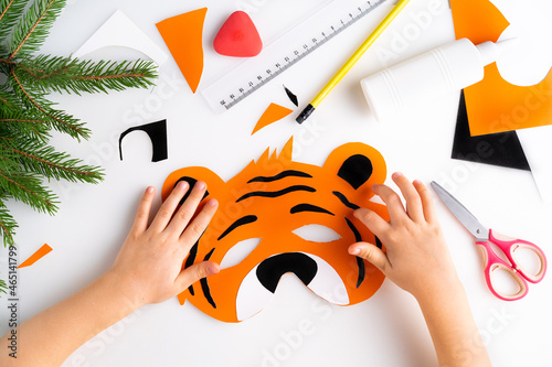the process of making a children's New Year tiger mask with a child made of colored paper, top view, symbol 2022, step 6