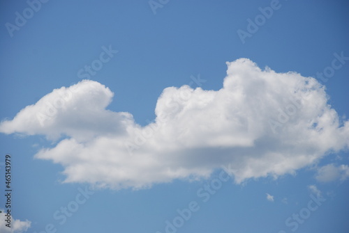 White fluffy cloud. Against the background of a clear light blue sky, a lonely large white cloud is somewhat reminiscent of a spaceship. The cloud is white at the top and gray at the bottom.