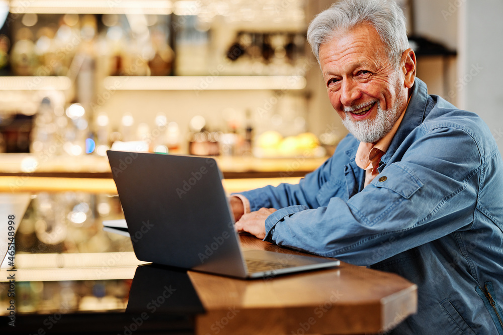 The happy senior student is sitting at his home and studying for an exam. Senior using the laptop for studying. The happy senior student is sitting at his home and studying for an exam. Senior using the laptop for studying.