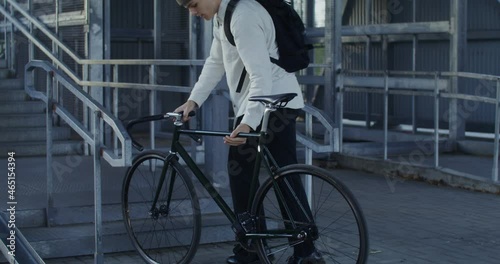A man rides a bicycle to ladder, takes bicycle in his arms and carries it up