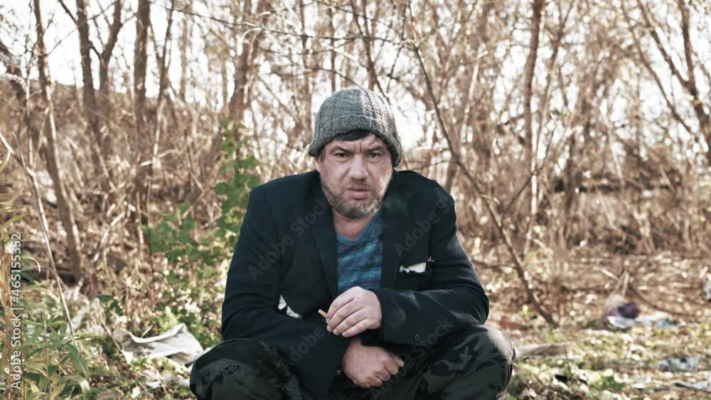 a homeless hungry man lightly dressed on the street in a torn suit smokes a cigarette an old beggar looks at the camera. a homeless hungry man lightly dressed on the street in a torn suit smokes a cigarette an old beggar looks at the camera.