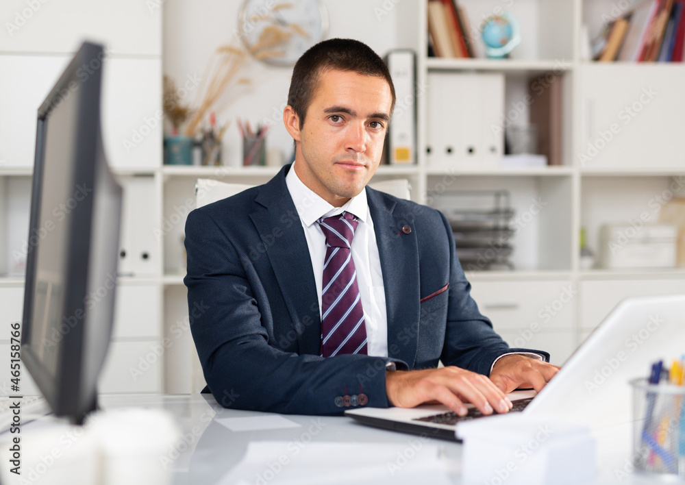 Portrait of confident focused office employee during daily work with laptop and documents