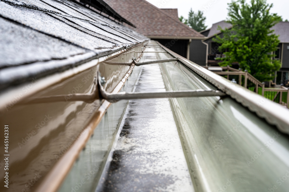 Selective focus on a section of residential guttering with hanger conveying water during a storm. Rain splatters and drops visible. Selective focus on a section of residential guttering with hanger conveying water during a storm. Rain splatters and drops visible.