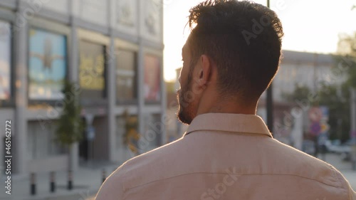 View from behind unrecognizable brunette man back view businessman guy in formal shirt tourist standing in city outdoors looking at urban buildings enjoying sunset sunlight male silhouette in sun rays