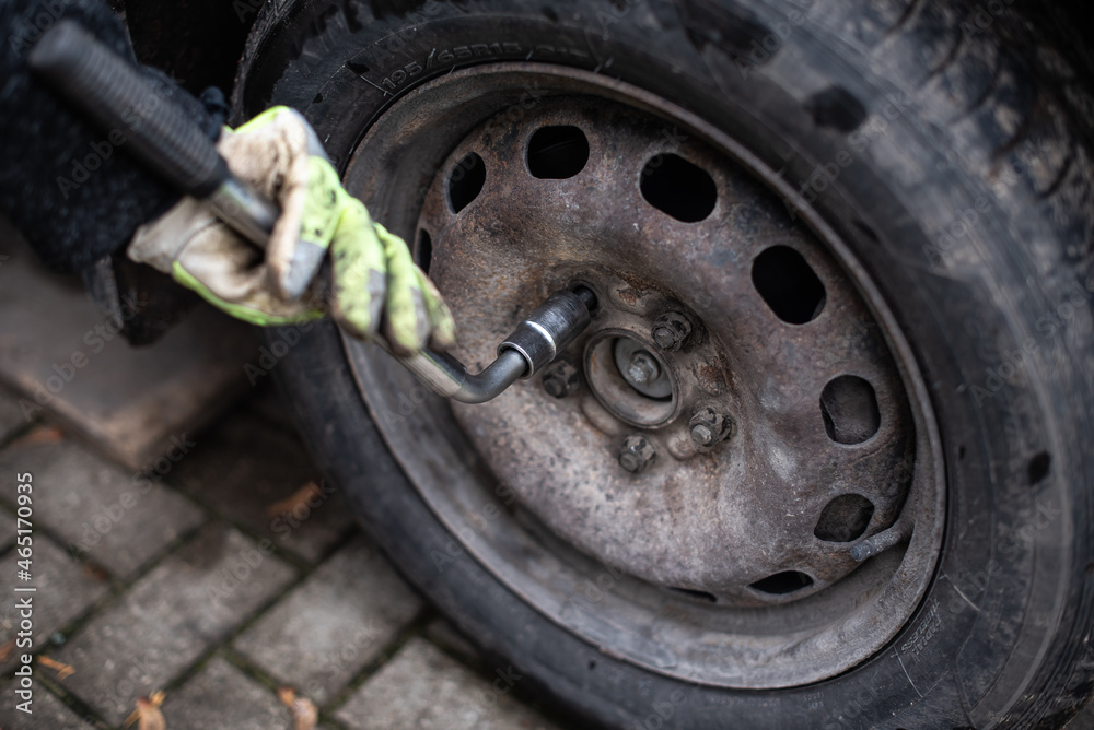 A man with wrench screw car wheel nut. Green dirty gloves in his hands. A man with wrench screw car wheel nut. Green dirty gloves in his hands.