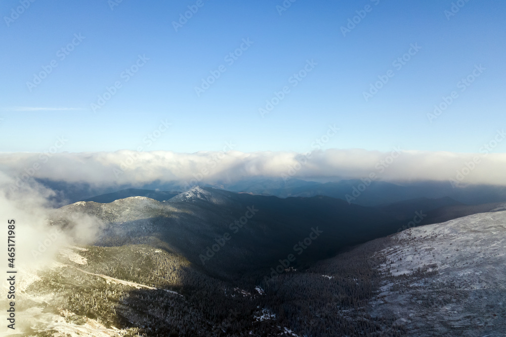 Fototapeta premium Aerial view from above of white puffy clouds covering snowy mountain tops in bright sunny day.