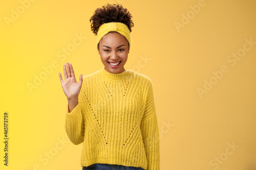 Cute timid friendly young girl wanna find new friends look pleasant smiling charmingly gladly waving hand hello hi gesture say welcome greeting heartwarming introduction herself, yellow background