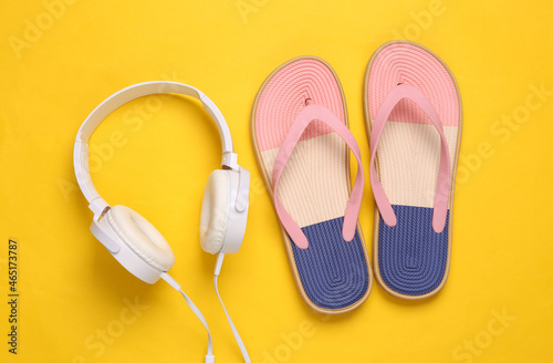 Colored flip flops with headphones on yellow background. Beach vacation concept. Flat lay
