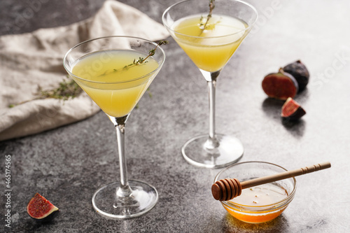 Two martini glasses with yellow non-alcoholic beverage lemonade with thyme branch, honey and figs on grey marble surface