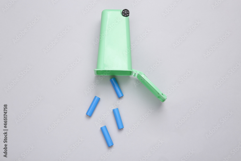 Battery recycling concept. Miniature trash can with aa batteries on gray background. Top view Battery recycling concept. Miniature trash can with aa batteries on gray background. Top view
