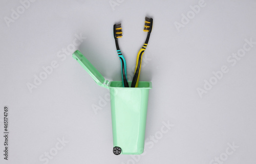 Plastic toothbrushes in mini trash can on gray background. Plastic free. Recycling concept. Top view. Flat lay