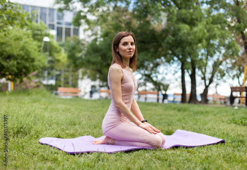 Attractive yogi woman sitting on mat and looking at camera in park