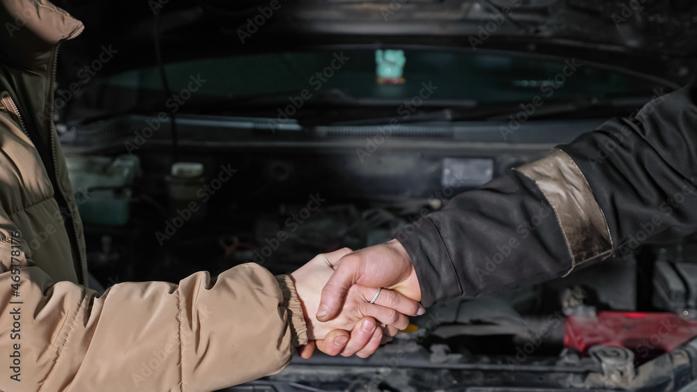 Skilled worker and woman client shake hands standing near broken automobile with open bonnet at modern car repair service station station closeup