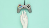 Mannequin hand touching retro gamepad on blue background. Top view. Creative art, minimalism