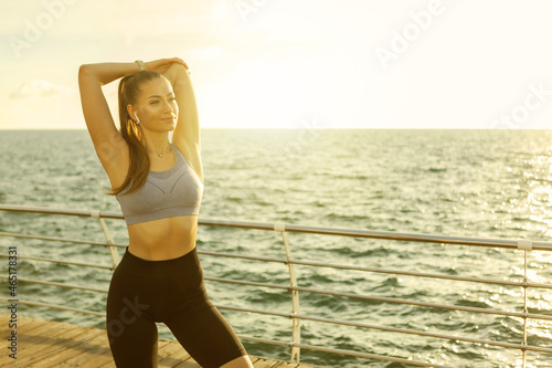 Slim fit woman with perfect body is practicing hand stretching before training on the beach at sunrise