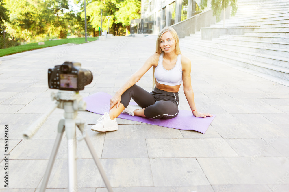 Sport blog. Attractive young sports woman talks to her followers about the benefits of outdoor exercise, records on camera on tripod. Lesson for her fitness vlog