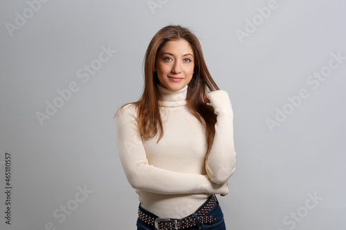 Portrait of a beautiful girl on an isolated gray background. Young brown-haired woman with loose long hair in a sweater and jeans.