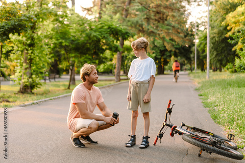 Ginger man talking with his son while teaching him how to ride bicycle
