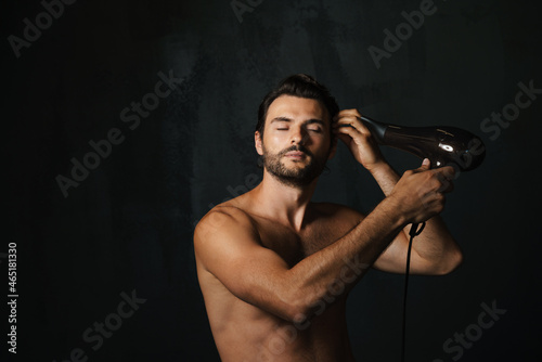 Young half-naked man posing on camera while using hair dryer