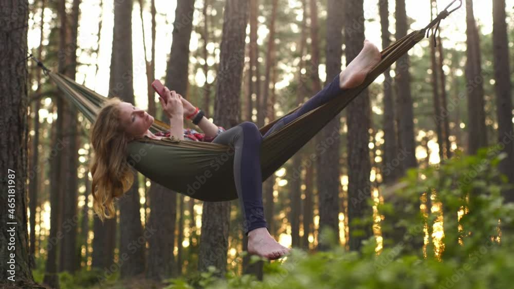 Beautiful blond haired girl looking at mobile phone in a hammock 