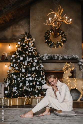 young beautiful woman model with long hair in a beige suit christmas tree christmas In brown wooden houses 