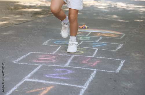 Little child playing hopscotch drawn with chalk on asphalt outdoors  closeup