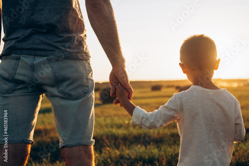 Father's and his son holding hands at sunset field. Dad leading son over summer nature outdoor. Family, trust, protecting, care, parenting concept