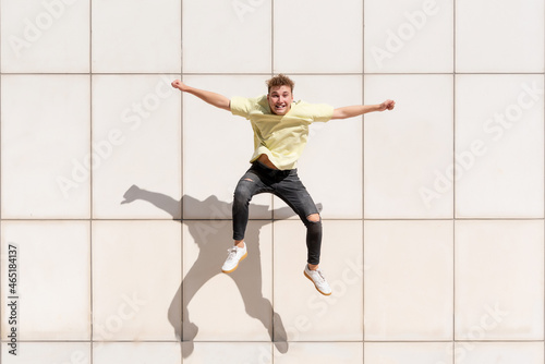 Young man in a yellow T-shirt with curly hair jumping and casting his shadow on a concrete wall