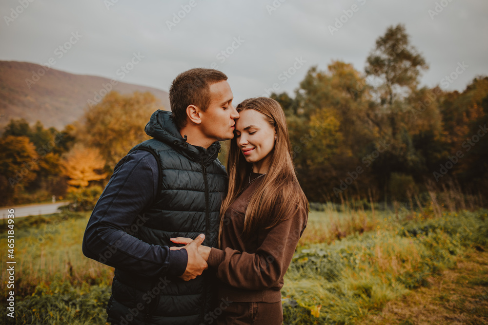 Man and woman hugging and kissing against autumn mountain forest Man and woman hugging and kissing against autumn mountain forest