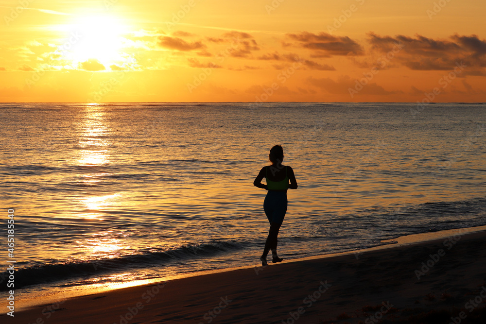 Silhouette of barefoot woman running by the sand in the sea waves in sunrise. Workout on a beach at early morning, healthy lifestyle