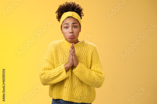 Silly cute pitty young african-american teenage daughter asking pocket money go trip press palms supplication pray need help begging make sad sulking miserable expression, standing yellow background photo