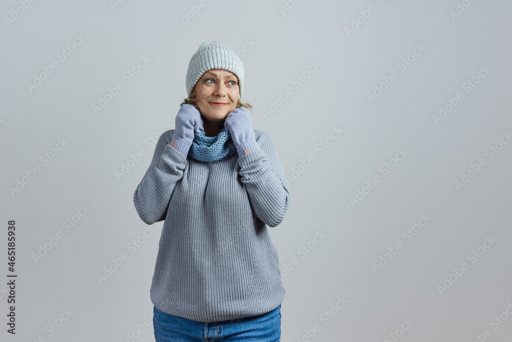 mature woman in a gray sweater and knitted hat wrapped herself in a scarf from the cold. Isolated on gray background mature woman in a gray sweater and knitted hat wrapped herself in a scarf from the cold. Isolated on gray background