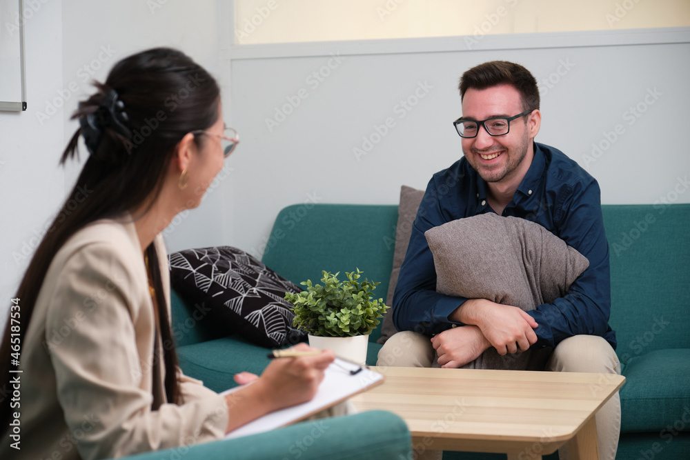 Asian female psychologist and caucasian man patient laughing at therapy. Asian female psychologist and caucasian man patient laughing at therapy.