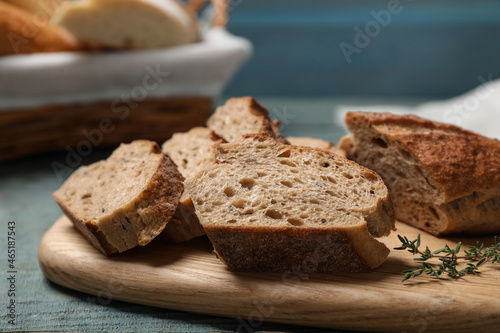 Cut buckwheat baguette with thyme on light blue wooden table  closeup