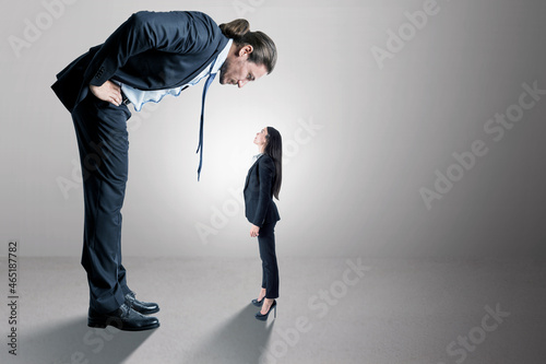 Businessman looking down on female subordinate on concrete background with mock up place for your advertisement. Boss and discrimination concept. photo