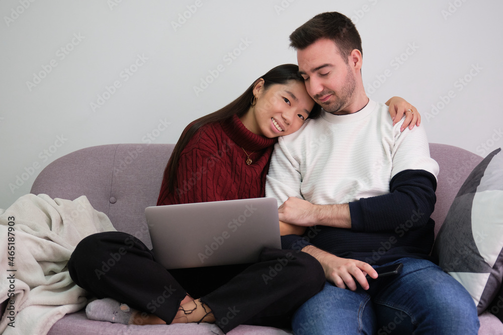 Young couple relaxing on a couch at home using laptop and embracing.