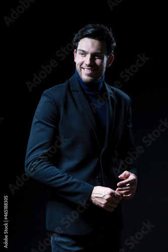 Smiling Handsome Caucasian Brunet Businessman Wearing Black Suit Posing With Folded Hands Looking Aside Against Black Studio Background. © danmorgan12
