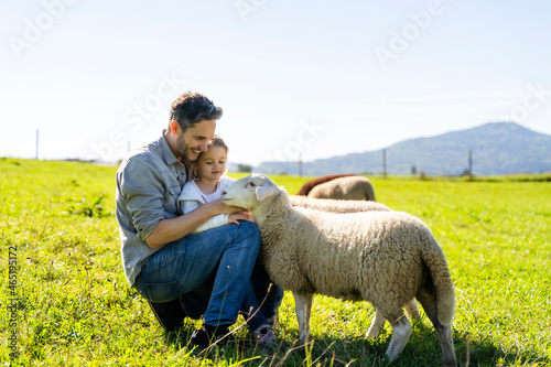 Smiling father and daughter stroking sheep in farm photo