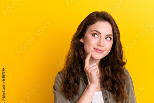 Photo of charming sweet young woman dressed brown shirt finger chin smiling looking empty space isolated yellow color background