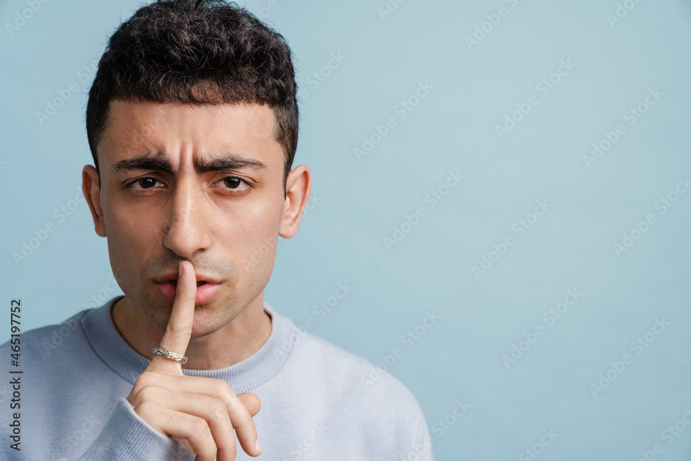 Young middle eastern man showing silence gesture at camera